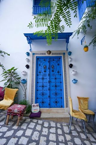 Una porta blu affascinante incorniciata da una vivace vegetazione e sedie di legno a Sidi Bou Said, Tunisia | MSC Crociere