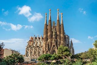 The stunning Sagrada Familia cathedral stands majestically against a bright blue sky, surrounded by lush greenery | MSC Cruises