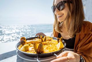 Une femme savoure une délicieuse paella tout en admirant la mer par une journée ensoleillée | MSC Croisières