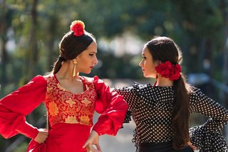 Deux femmes en robes de flamenco traditionnelles se sourient l'une à l'autre dans une rue ensoleillée | MSC Croisières