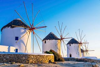 Drei ikonische Windmühlen vor einem lebhaften Himmel während des Sonnenuntergangs, der den Charme von Mykonos in Griechenland symbolisiert | MSC Cruises