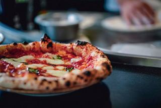 Une délicieuse pizza garnie d'ingrédients frais, une main prépare la pâte en arrière-plan | MSC Croisières