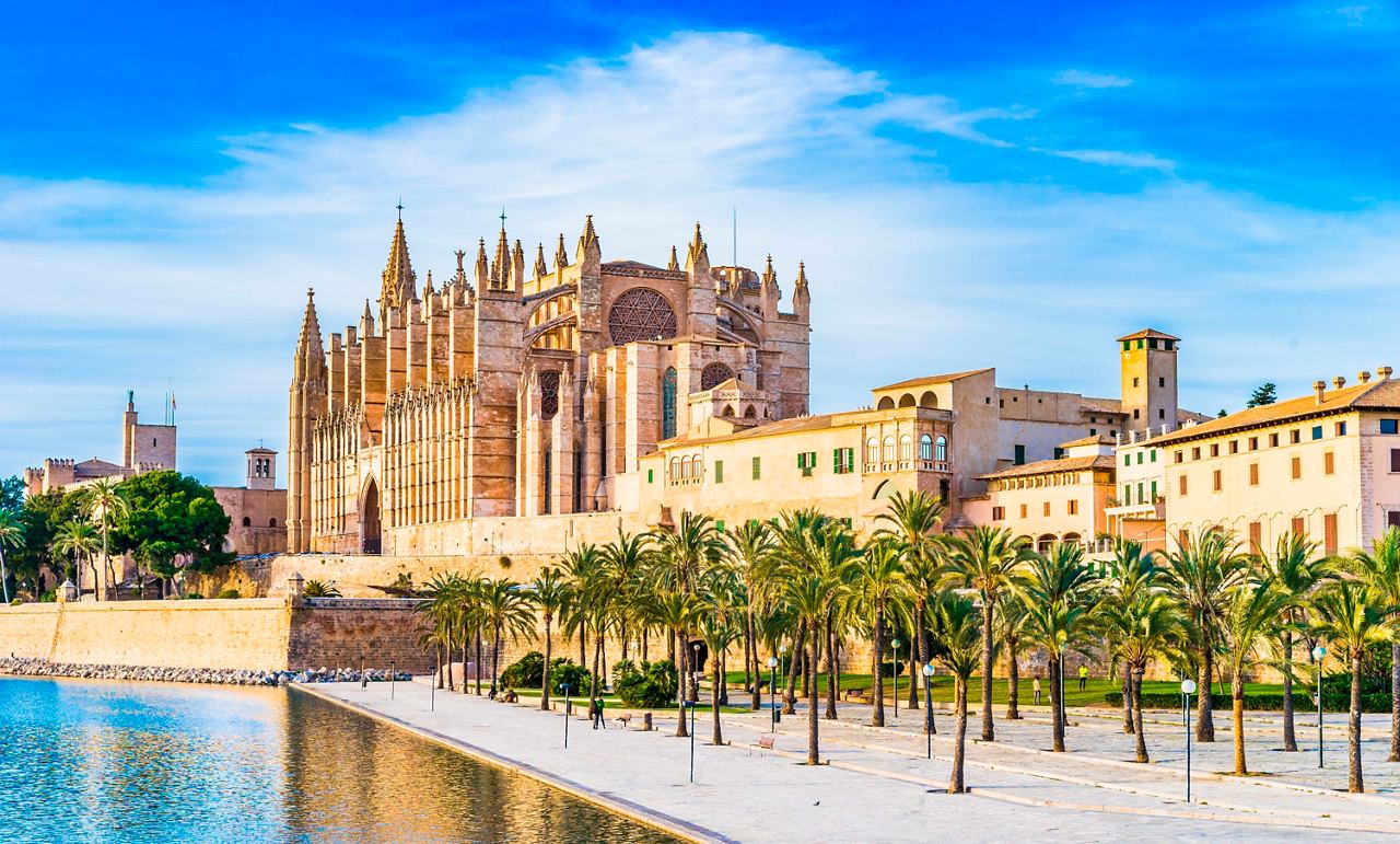 The stunning Cathedral of La Seu stands majestically by the water in Palma de Mallorca, surrounded by palm trees | MSC Cruises