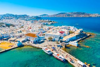 Aerial view of Mykonos showcasing the vibrant coastline and bustling port area under a clear blue sky | MSC Cruises