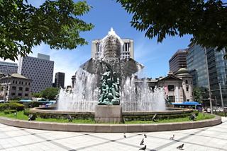 Una hermosa fuente con una estatua de bronce rodeada de árboles y edificios en Busan, Corea del Sur | MSC Cruceros