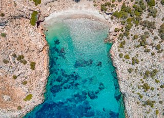 Aerial view of Armeas Beach in Syros, Greece, showcasing turquoise waters surrounded by rocks and lush vegetation | MSC Cruises