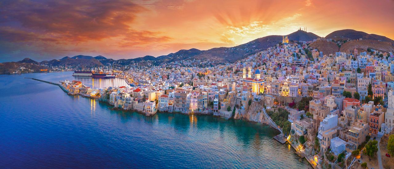 Une vue panoramique d'Ermoupoli, Syros, avec la côte, la mer et un beau ciel au coucher du soleil | MSC Cruises