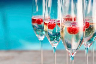 Elegant glasses of champagne with raspberries perched on the rim, set against a vibrant pool backdrop | MSC Cruises