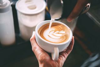 A hand holds a warm cappuccino topped with frothy milk in an inviting café setting | MSC Cruises