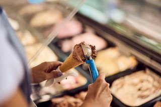 A person holds an ice cream cone while selecting flavours from a display of ice cream | MSC Cruises