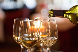 A hand pours white wine into glasses next to a glowing candle, creating a warm atmosphere | MSC Cruises