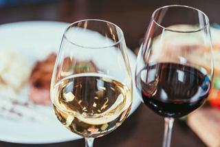 Two elegant wine glasses filled with red and white wine beside a plate of gourmet food in a restaurant setting | MSC Cruises