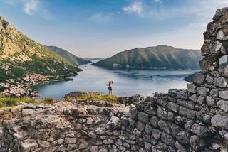 A woman stands near ancient ruins overlooking the serene waters of Kotor, Montenegro, surrounded by majestic mountains | MSC Cruises