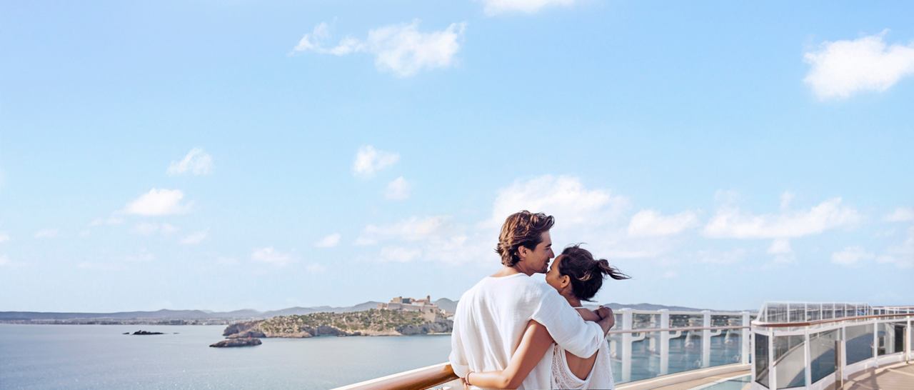 Ein Paar genießt einen romantischen Moment an einem Geländer mit Blick auf das Meer und einen klaren blauen Himmel | MSC Cruises