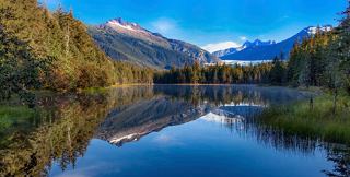 A serene lake reflects the stunning mountains and sky in Mendenhall, Alaska, surrounded by lush vegetation | MSC Cruises