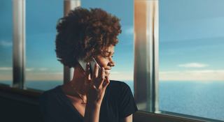 A woman enjoying her time on board, using a smartphone with a beautiful view in the background | MSC Cruises
