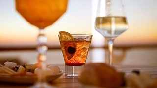 Colourful cocktails and glasses of wine with snacks, set against a serene sunset backdrop | MSC Cruises