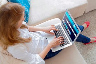 A woman sits on a sofa, using a laptop to explore and book travel options online | MSC Cruises