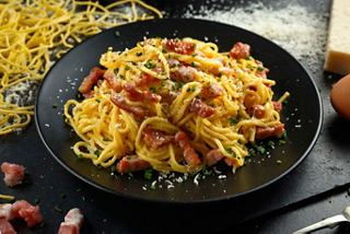 Une délicieuse assiette de pâtes Carbonara garnie de bacon et d'herbes, illustrant la tradition culinaire italienne | MSC Croisières