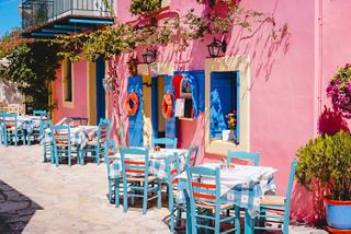 A vibrant Mediterranean street scene in Corfu featuring colourful buildings, outdoor seating, and blooming flowers | MSC Cruises
