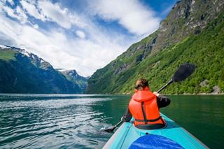 A woman kayaking on serene waters surrounded by lush mountains in Geirangerfjord, Norway | MSC Cruises