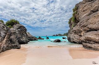 A serene view of Horseshoe Bay Beach framed by rocks and gentle waves under a cloudy sky | MSC Cruises