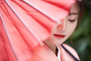 A woman gracefully holds a vibrant pink umbrella, surrounded by lush greenery in a serene setting | MSC Cruises