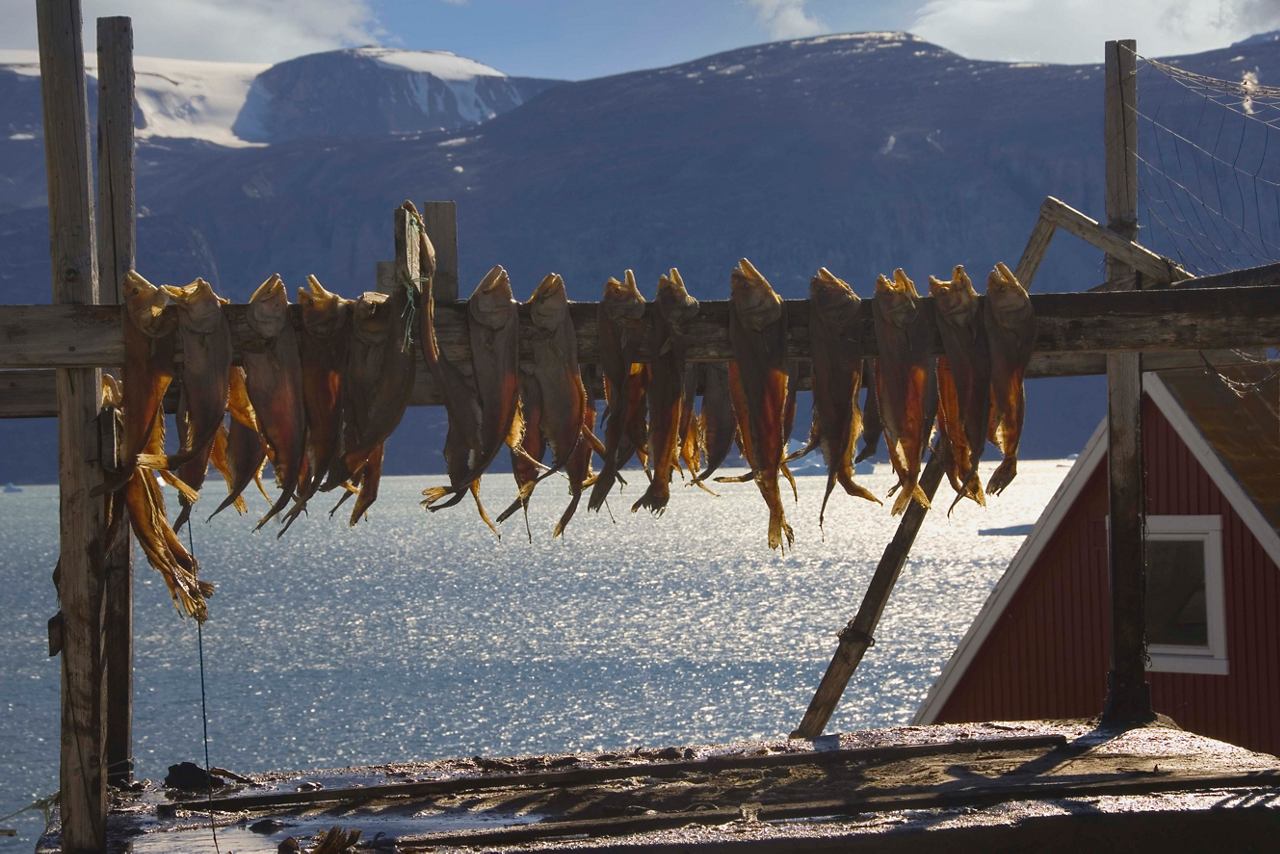 Dried fish hangs between wooden beams, with mountains and a serene sea in the background | MSC Cruises