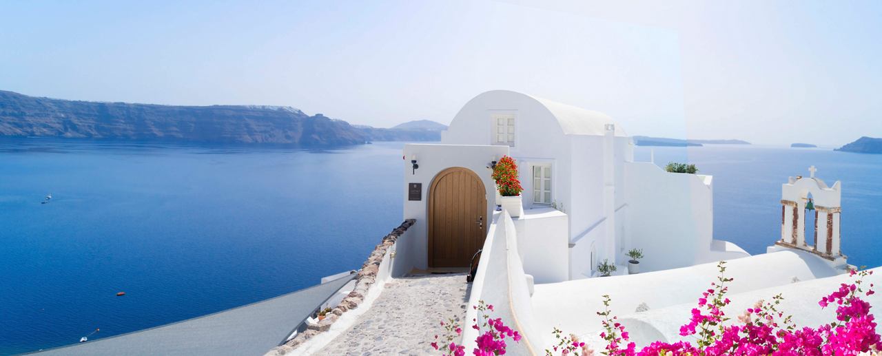 Una vista serena de Santorini con arquitectura blanca, flores vibrantes y un mar tranquilo bajo un cielo claro | MSC Cruises