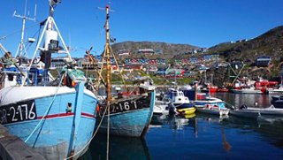 Bateaux colorés amarrés dans un port pittoresque entouré de montagnes sous un ciel bleu clair à Qaqortoq, Groenland | MSC Croisières