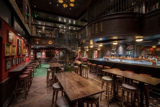 A warm and inviting pub interior featuring a double-deck layout, winding staircase, and a bar counter | MSC Cruises