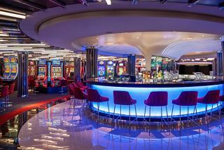 A vibrant casino bar with glowing blue accents and seating, inviting guests to enjoy entertainment on MSC World Asia | MSC Cruises