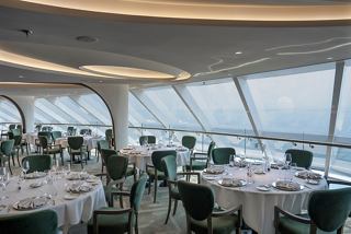 A beautifully arranged dining area with panoramic views of the sea through glass walls at the MSC Yacht Club Restaurant | MSC Cruises