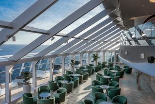 A serene dining area with green furnishings and glass walls, offering stunning views of the sea | MSC Cruises