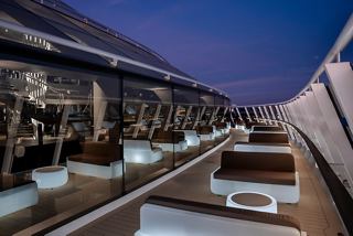 A serene sitting area with outdoor furniture and a glass wall, inviting relaxation during dusk at the MSC Yacht Club | MSC Cruises