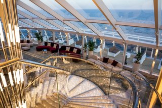 A spacious sitting area in the Top Sail Lounge featuring elegant sofas, a glass wall, and stunning views of the ocean | MSC Cruises
