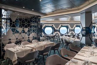 A stylish dining area featuring tables and chairs with portholes offering views of the sea and sky | MSC Cruises