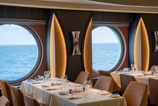 A dining area with tables and chairs, featuring round portholes that overlook the sea | MSC Cruises