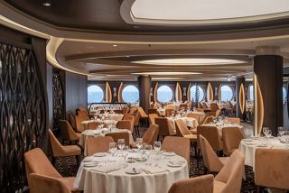 Elegant dining area with tables and chairs, featuring portholes offering views of the sea | MSC Cruises