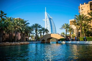 A serene view of Dubai's skyline with a prominent skyscraper, palm trees, and a tranquil sea | MSC Cruises