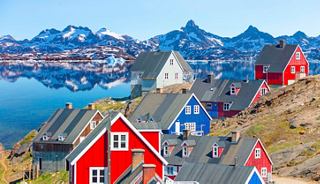 A picturesque village in Greenland featuring vibrant buildings against a backdrop of majestic mountains and a clear blue sky | MSC Cruises