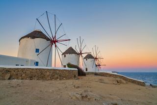 Windmills stand against a vibrant sunset backdrop in Mykonos, Greece, creating a picturesque Mediterranean scene | MSC Cruises