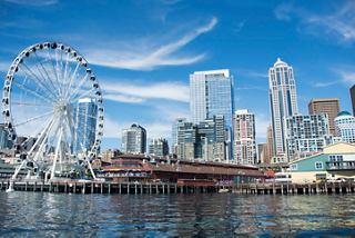 Eine lebendige Skyline von Seattle mit modernen Wolkenkratzern und einem Riesenrad, das über die Elliott Bay unter einem klaren blauen Himmel blickt | MSC Cruises