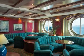 A welcoming lounge area featuring comfortable seating, a table, and a view through a large porthole | MSC Cruises