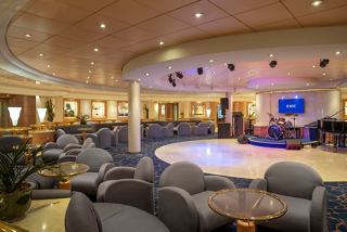 A stylish lounge area with comfortable seating, a stage, and a piano, inviting guests to relax and enjoy entertainment | MSC Cruises
