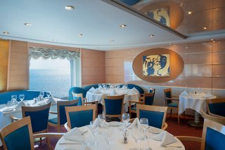 Elegant dining area with round tables and plush chairs, featuring portholes and warm decor | MSC Cruises