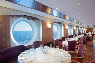 A welcoming dining area with elegant tables and chairs, featuring views through large portholes of the sea | MSC Cruises