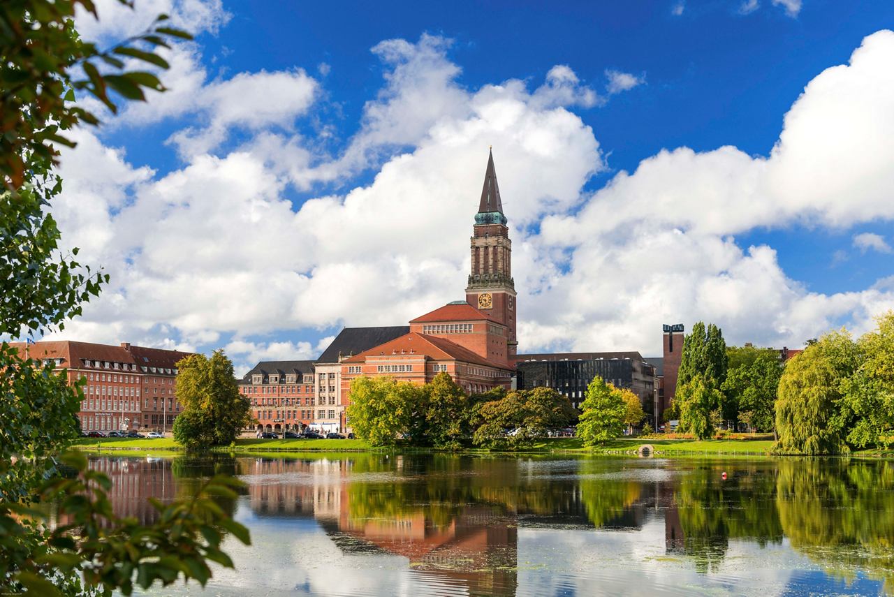 Une vue pittoresque de l'hôtel de ville de Kiel reflétée dans l'eau, entourée d'arbres luxuriants et d'un ciel bleu | MSC Cruises