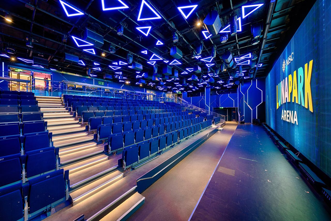 A spacious seating area in the MSC Luna Park Arena, featuring vibrant lighting and a large screen for entertainment | MSC Cruises