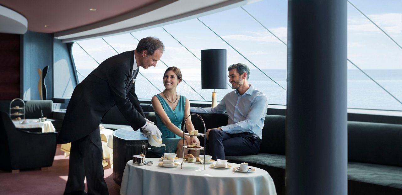 Una pareja disfruta de un té de la tarde servido por un mayordomo en el elegante Top Sail Lounge con vistas panorámicas al mar | MSC Cruises